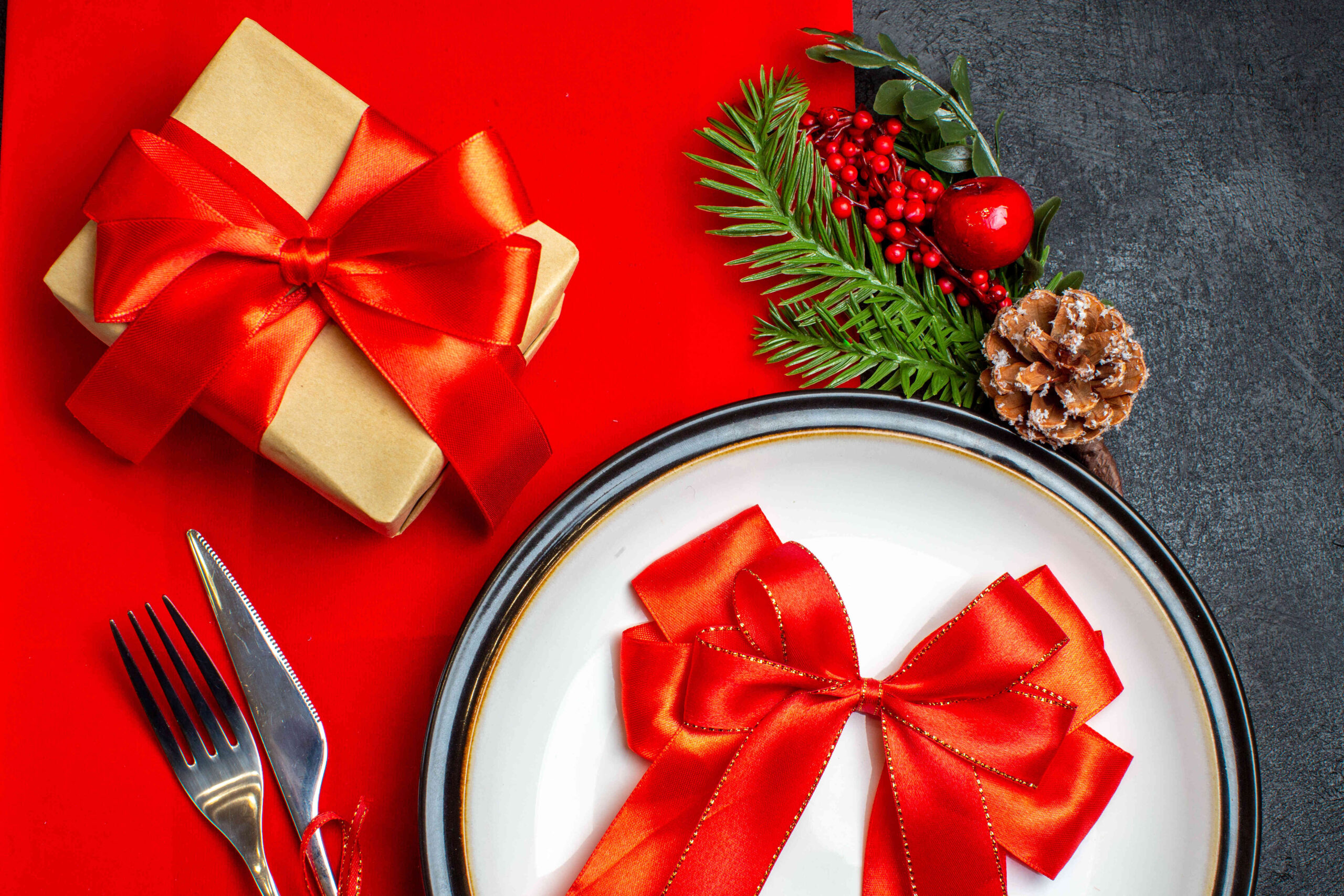 overview-new-year-background-with-red-ribbon-dinner-plate-cutlery-set-decoration-accessories-fir-branches-gift-red-napkin_optimized